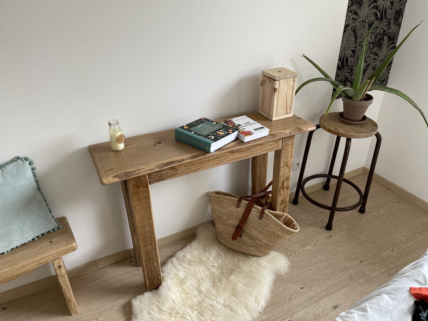 Banc d'entrée en bois massif clair, panier et livres posés dessous, sur tapis en peau